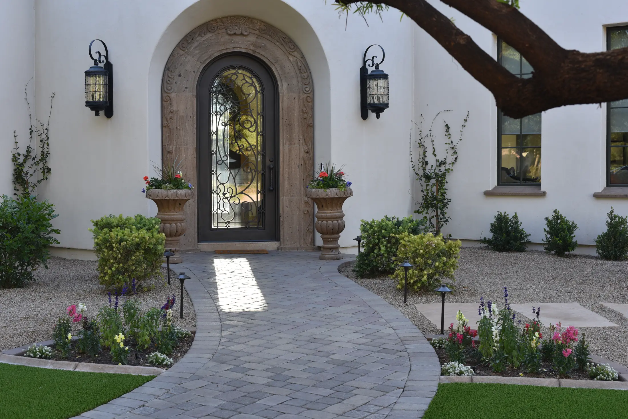 Finished front landscape with a curved paver walkway, stone urn planters, flower beds, and layered plantings
